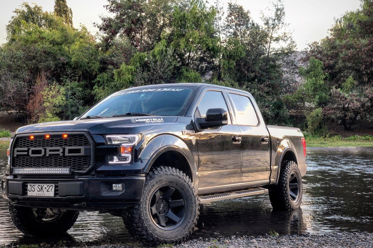 A Ford with offset wheels driving through a shallow lake